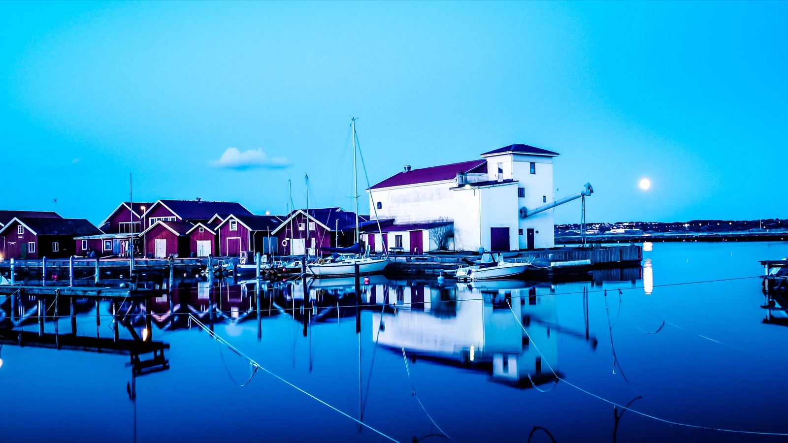 Björkö hamn i blå skymning med månen över sjöbodarna