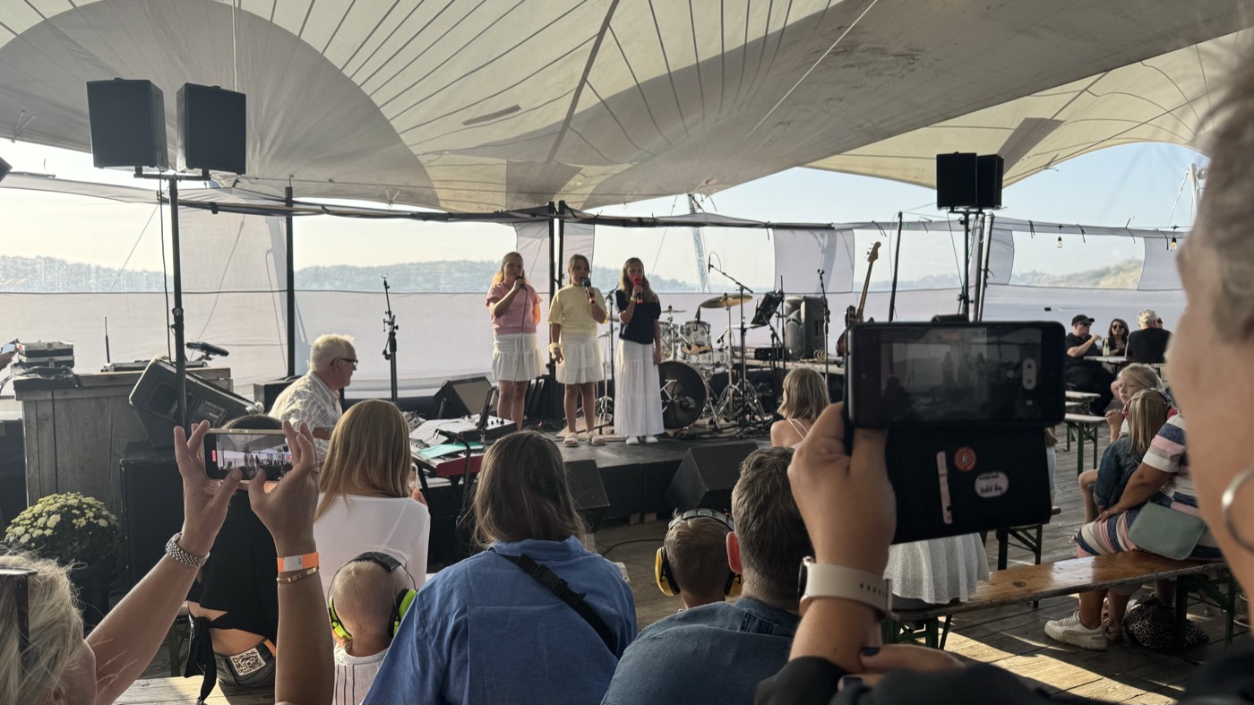 Tre unga sångerskor på tältscen med havet och skärgården i bakgrunden